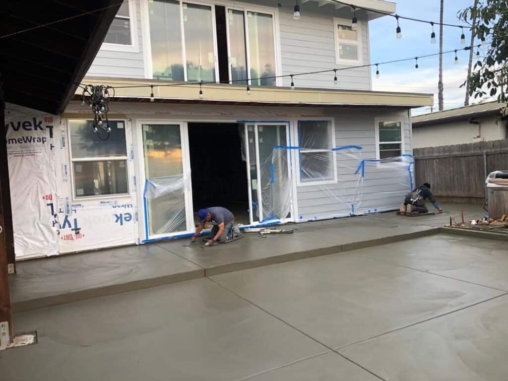 Workers pouring and smoothing concrete on backyard patio.